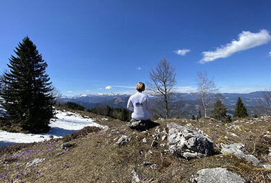 Sodelavka sedi na kamnu in opazuje razgled na dolino in hribe.