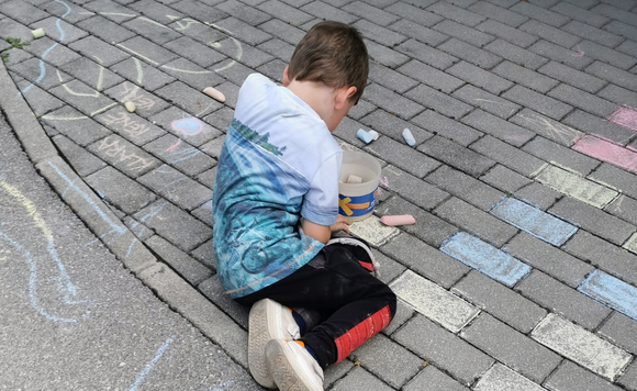 Otrok z barvnimi kredami riše po tleh.
