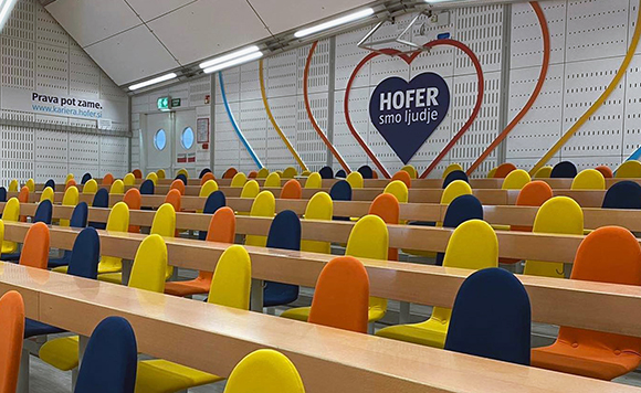 HOFER predavalnica na EF z rumenimi, oranžnimi in temno modrimi stoli ter srčkom HOFER smo ljudje.